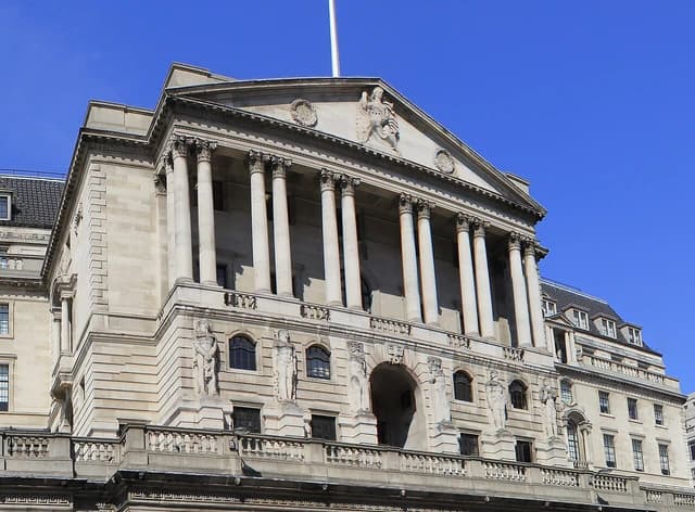 Bank of England building with classical columns and sculptures, under a clear blue sky.