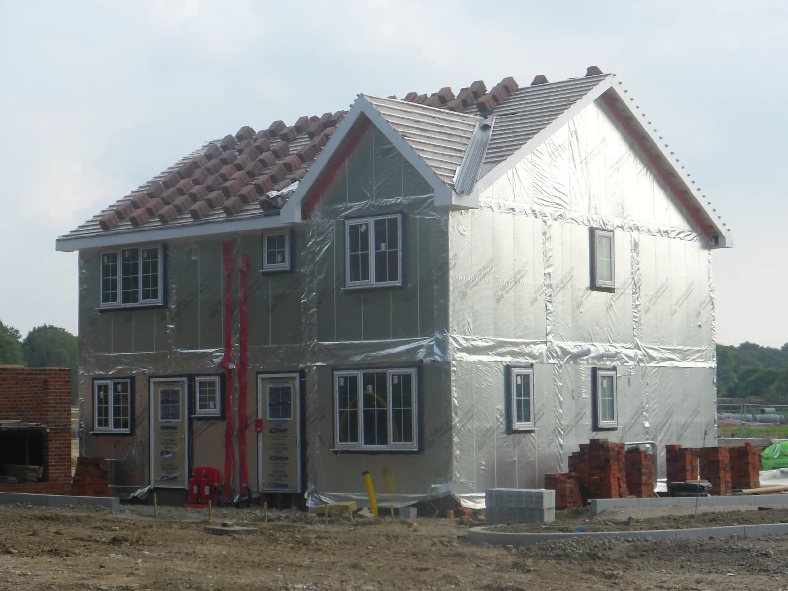 House under construction with insulation, roof tiles partially installed, and building materials nearby.