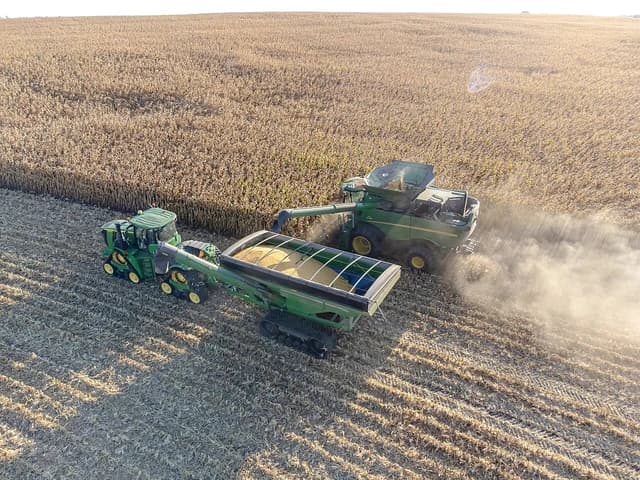 Combine harvester offloading corn into a grain cart in a field.