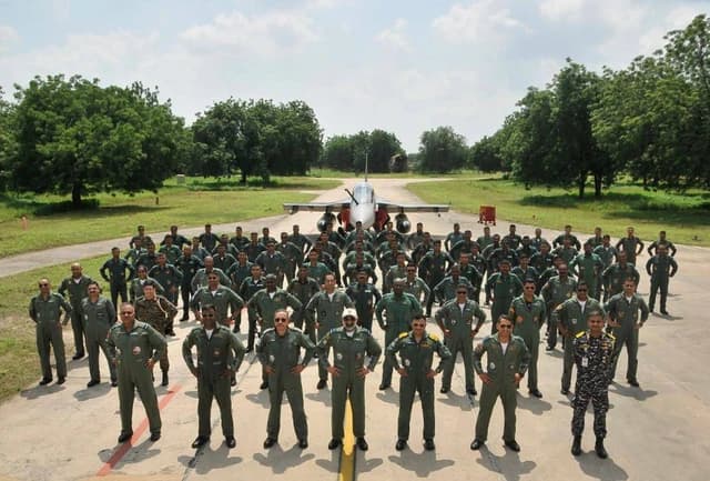 Indian Air Force and Navy personnel stand on an airfield in front of a Tejas fighter jet.