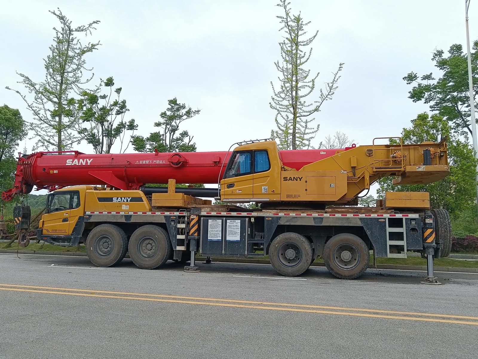 Sany mobile crane, red and yellow, parked on the side of a road.