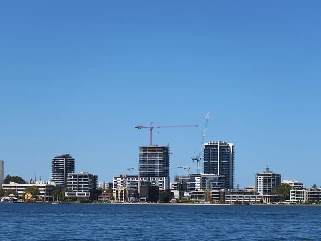 Skyline of South Perth, Australia, with residential buildings and construction cranes along the water.