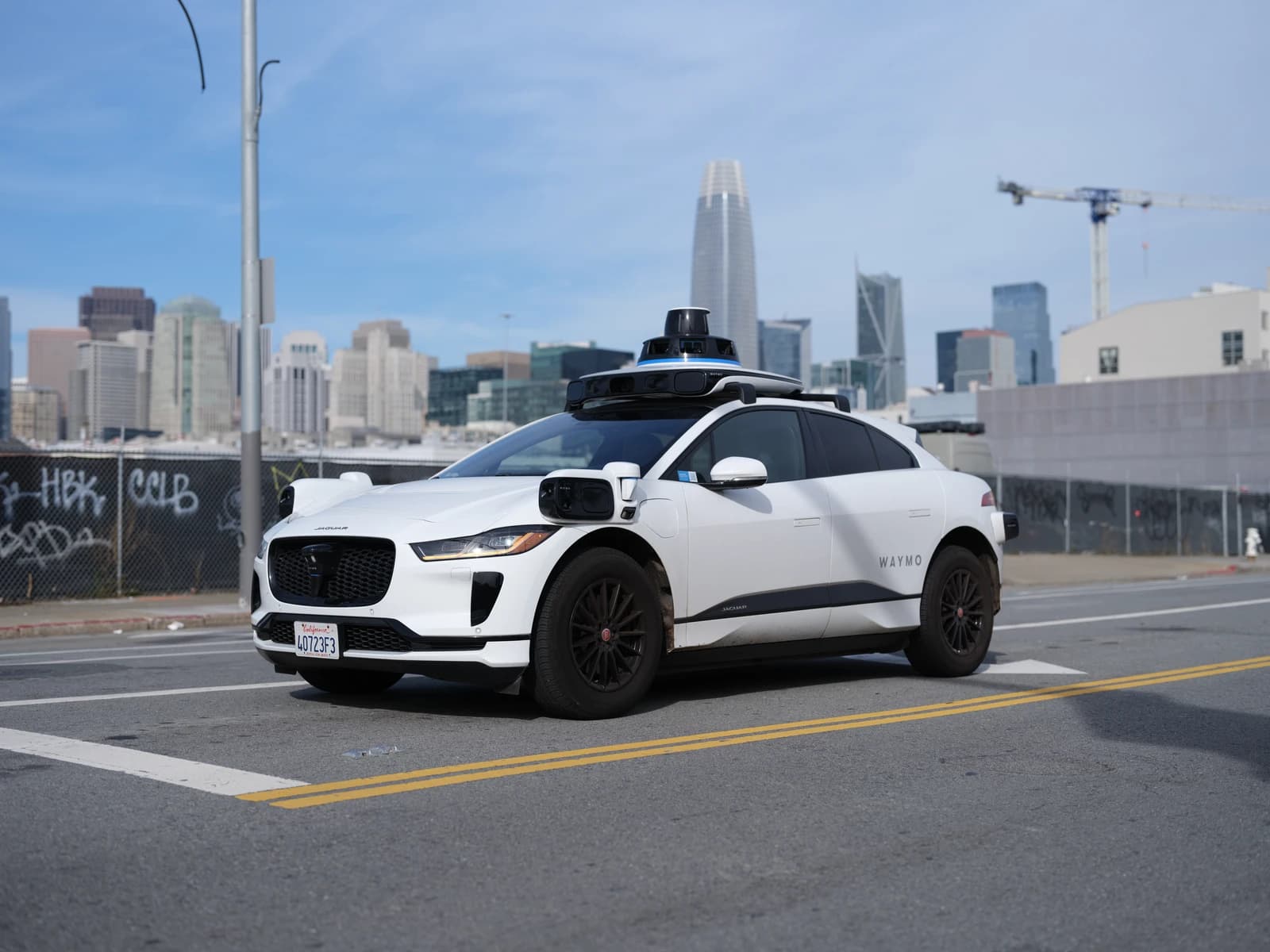 A white Waymo Jaguar I-Pace driverless taxi drives down a street in San Francisco.