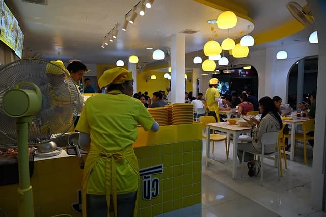 Restaurant staff in yellow uniforms serving customers at tables in a brightly lit dining area.