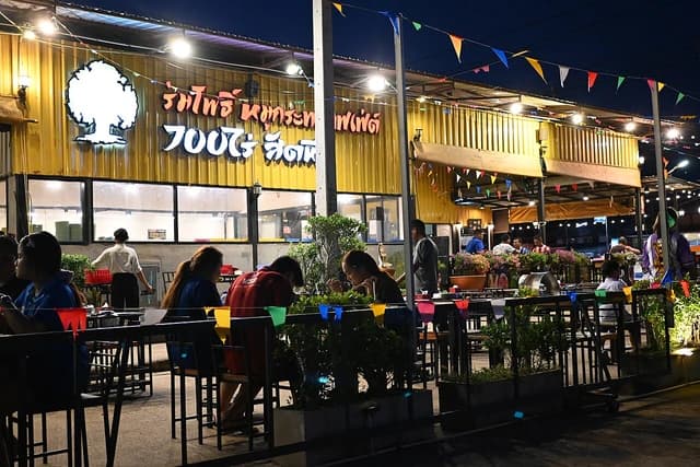 People eat and converse at outdoor tables in a brightly lit restaurant.