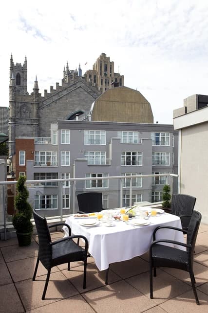 Private terrace set with breakfast, overlooking a city skyline with historic and modern buildings.
