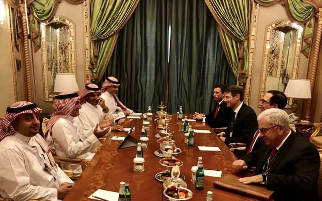 Steven Mnuchin and Yasir Al-Rumayyan at a large table with other individuals during a meeting.