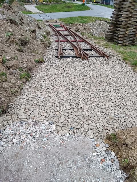 Railway tracks laid on gravel ballast with construction dirt piles nearby.
