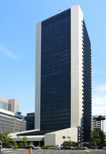 Mizuho Bank Head Office building in an urban setting, cars on a street nearby.