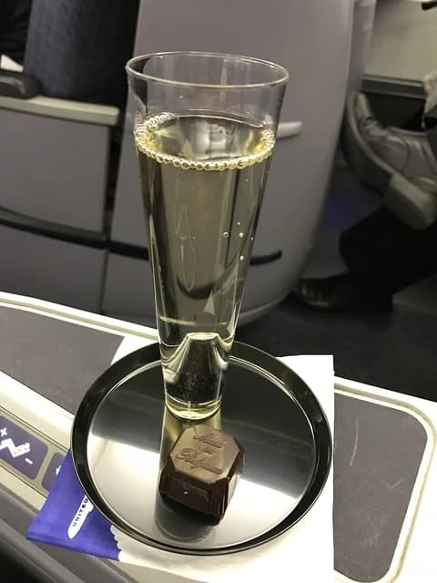 A glass of sparkling wine and a chocolate on a small tray inside an airplane cabin.