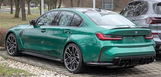 Green BMW M3 Competition sedan parked, showing the rear and side profile.