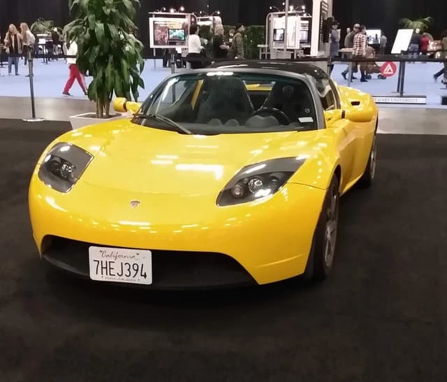 Yellow Tesla Roadster electric sports car on display indoors.