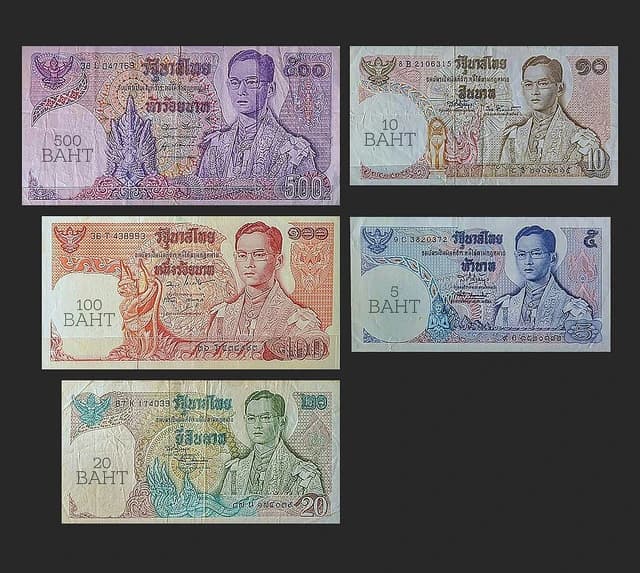 Five different Thai baht banknotes laid out on a dark background.