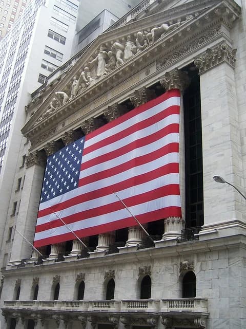 Neoclassical facade of the New York Stock Exchange building, with a large American flag draped across it.