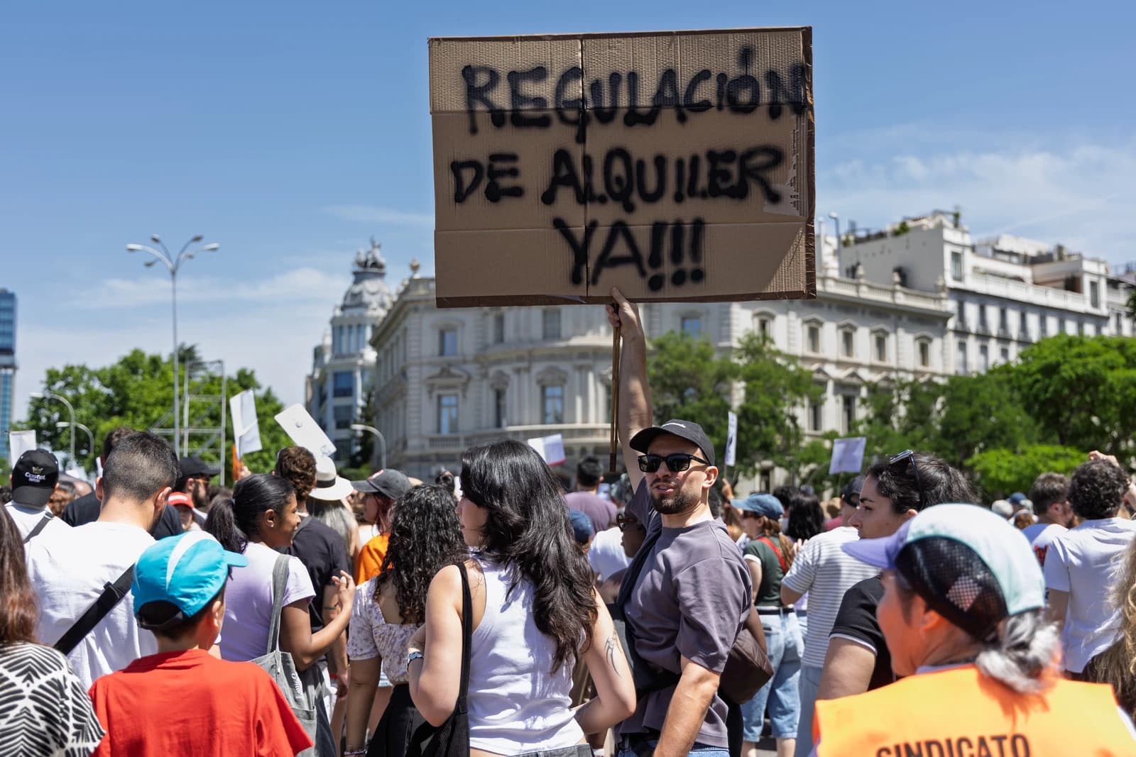 Man holding sign reading "Regulación de alquiler ya" at housing demonstration in Madrid.