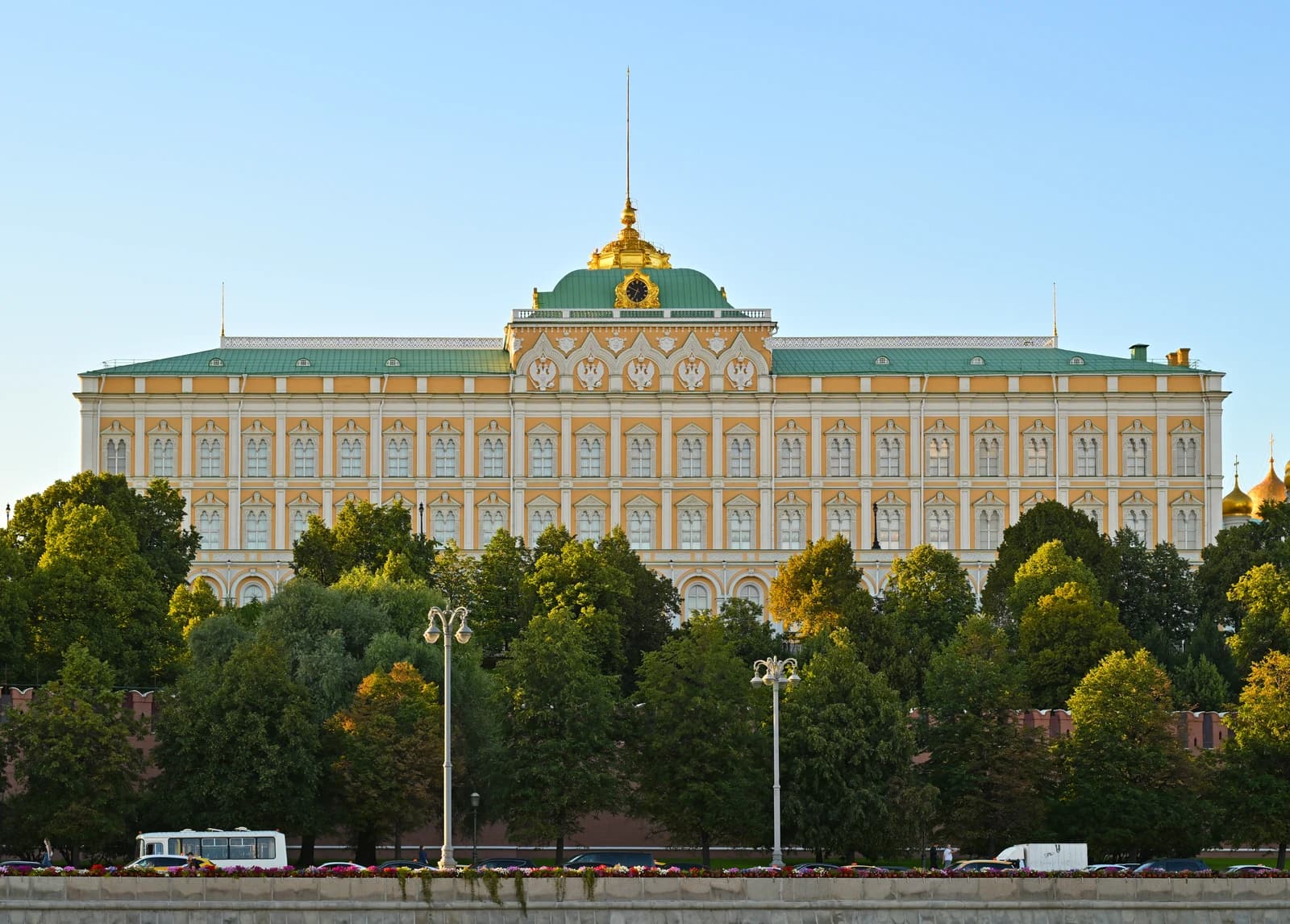 Grand Kremlin Palace, a large historical building, stands among green trees under a clear sky.