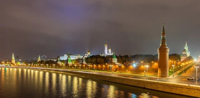 Illuminated Moscow Kremlin complex and Moskva River at night, showing towers and cathedrals.