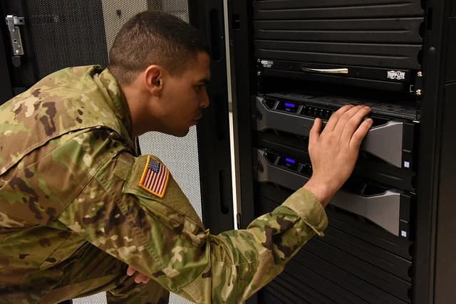 U.S. Army Soldier inspecting server equipment at a satellite communications operations center.