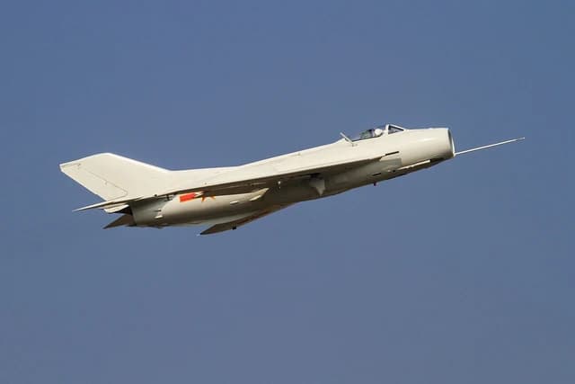 Shenyang J-6 fighter jet flying against a clear blue sky.