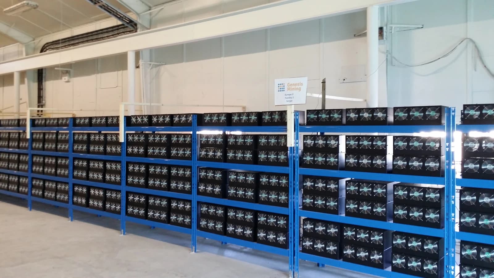 Rows of cryptocurrency mining machines with cooling fans in a large facility.