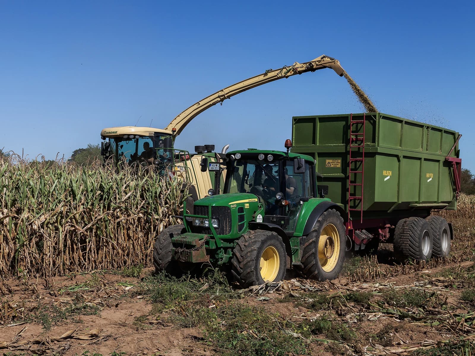 Tractor pulling a trailer while a combine harvester fills it with corn.