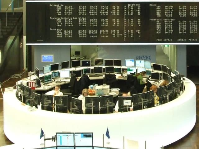 People sitting at desks with multiple computer monitors in a stock trading room.