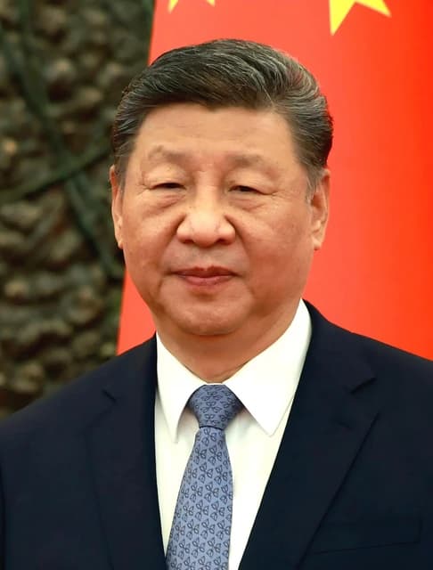 Xi Jinping, President of China, looking towards the camera with a red flag behind him.
