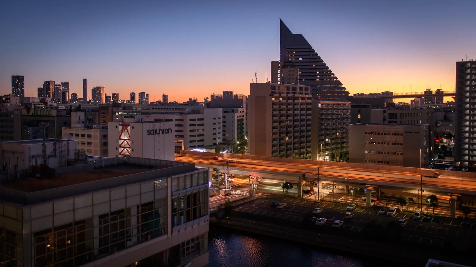 Twilight cityscape of Shibaura, Tokyo, showing buildings, elevated highways, and a canal.