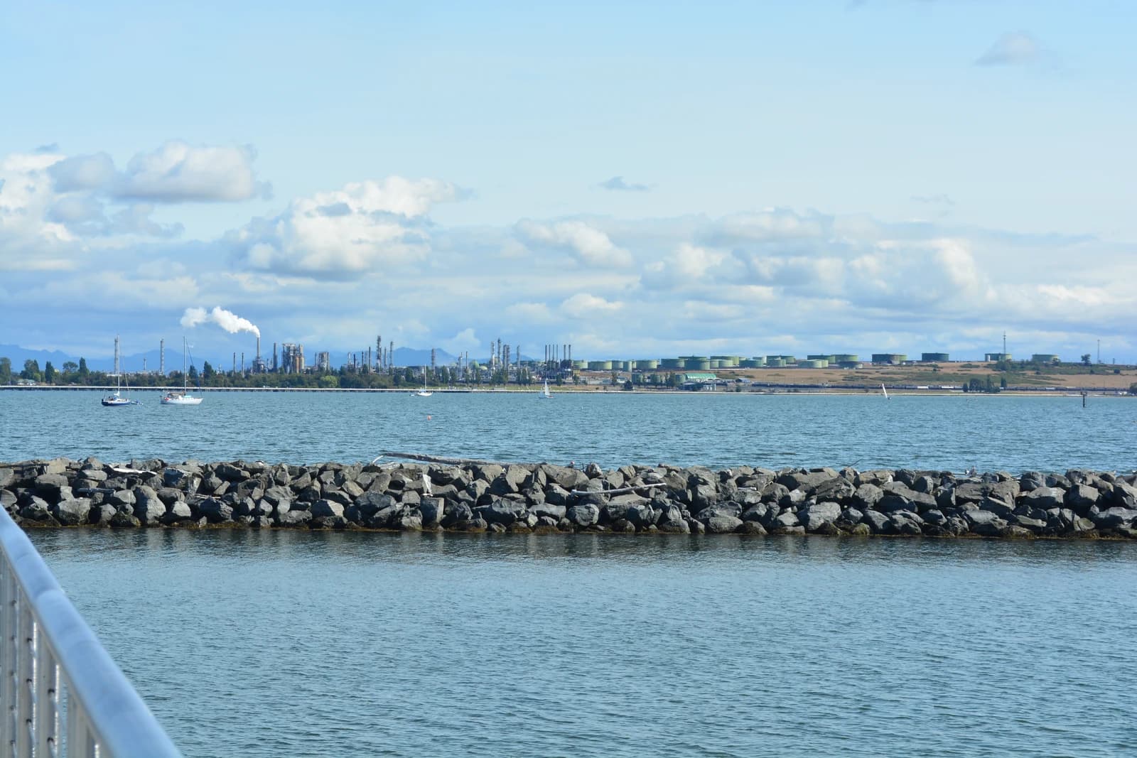 Oil refinery with smoke stacks and storage tanks along a distant coastline.