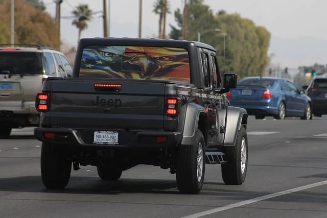Dark grey Jeep Gladiator JT pickup truck with an American flag bald eagle decal on its rear window driving on a street.