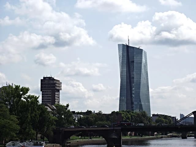 The glass and steel skyscraper of the European Central Bank stands tall against a cloudy sky.