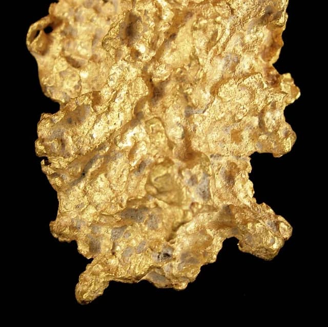 A close-up image of a rough, natural gold nugget against a black background.