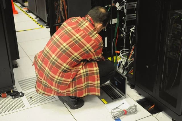 Technician working with a laptop on a server rack in a data center.