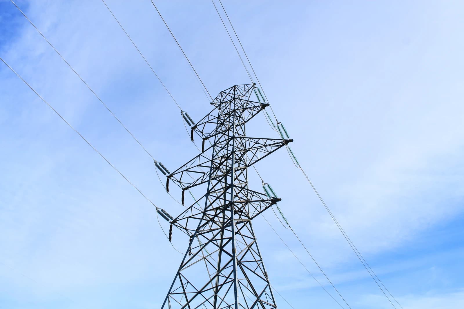 A large metal transmission tower holds multiple power lines against a clear blue sky.