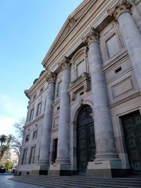 Massive stone building with large columns and an arched entrance, under a clear blue sky.