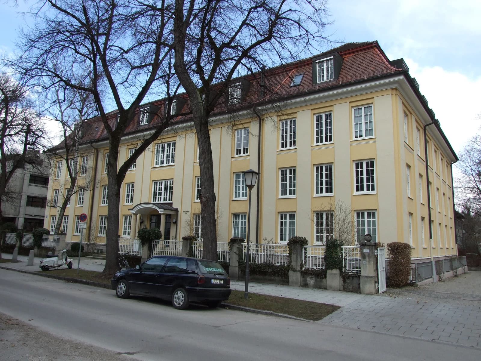 Exterior of the IFO Institute building with trees and parked cars.