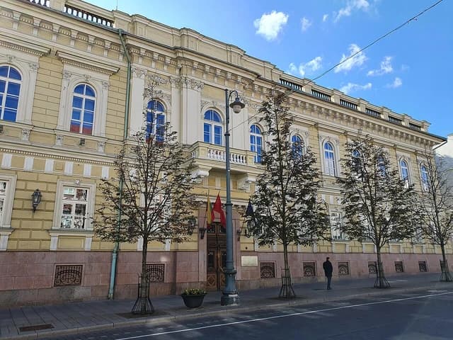 Central Office of the Bank of Lithuania building with trees and a sidewalk.