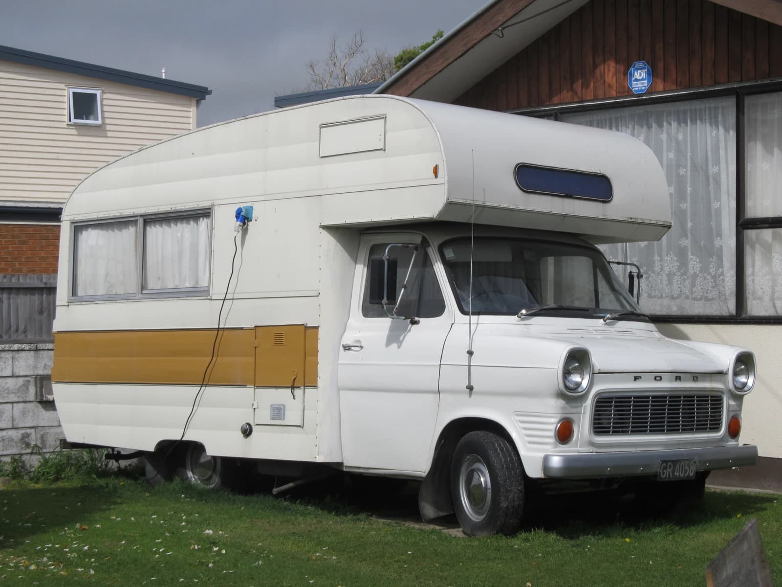 A vintage 1973 Ford Transit campervan, white with a tan stripe, parked outdoors.