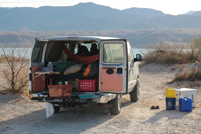 Camper van with open rear doors, camping gear visible inside, parked near a lake.