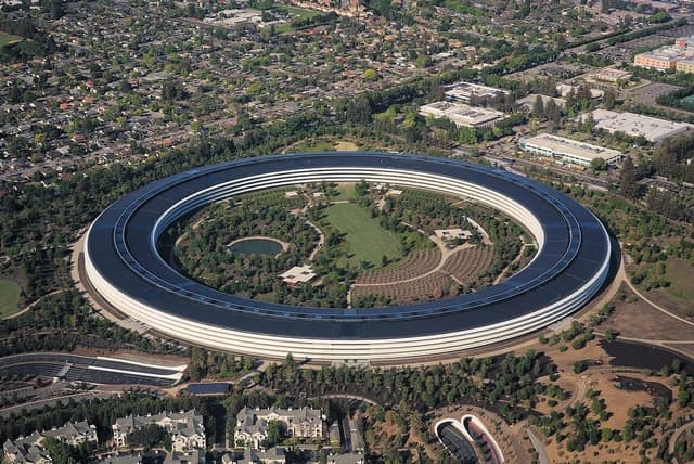 Aerial view of Apple Park headquarters, a large circular building surrounded by trees.