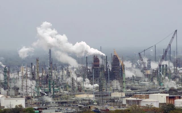 Exxon Mobil oil refinery complex in Baton Rouge, Louisiana, with smoke billowing from smokestacks.