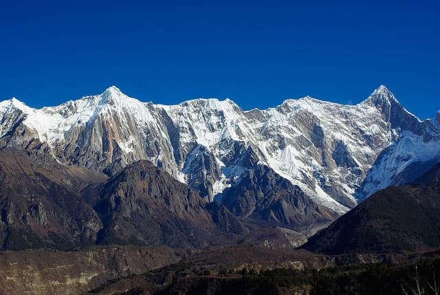 Snow-capped peaks of the Namcha Barwa mountain range in Tibet under a clear blue sky.