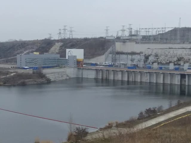 Tashlyk Pumped-Storage Power Plant with buildings, dam, and power lines on a gray day.