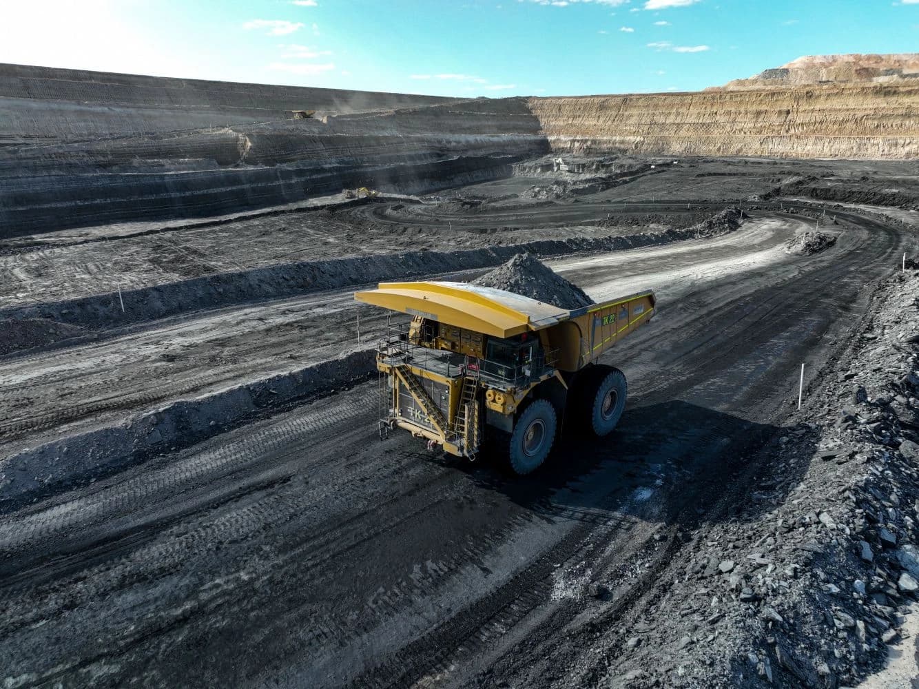Large yellow dump truck carrying a load of coal through an open-pit mine.