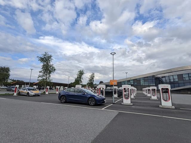 Multiple Tesla vehicles parked at charging stations under a cloudy sky.