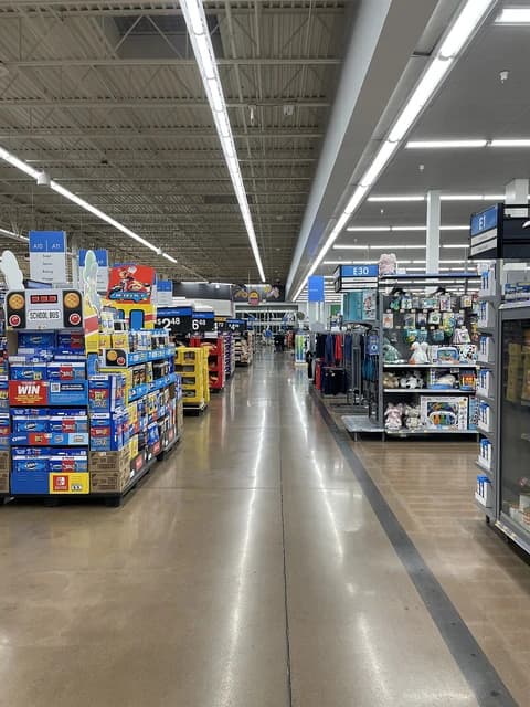 Interior of a Walmart Supercenter showing brightly lit aisles with merchandise on shelves and display boxes.