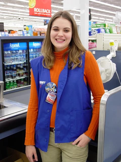 A Walmart cashier stands smiling at a checkout counter in a store.