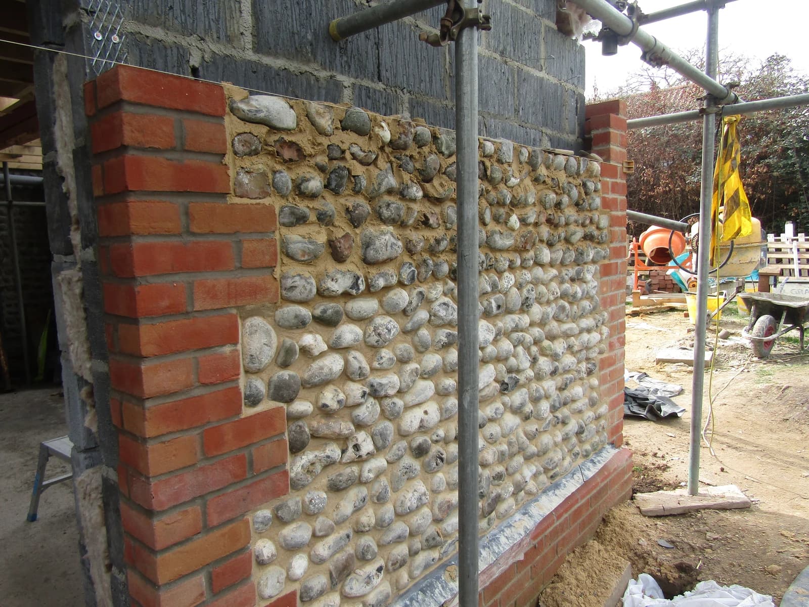 A partially constructed wall of a house, showing brick and flint work.