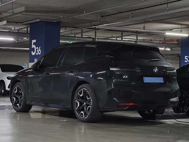 A black BMW iX xDrive50 Sport electric SUV parked and charging in an underground parking garage.