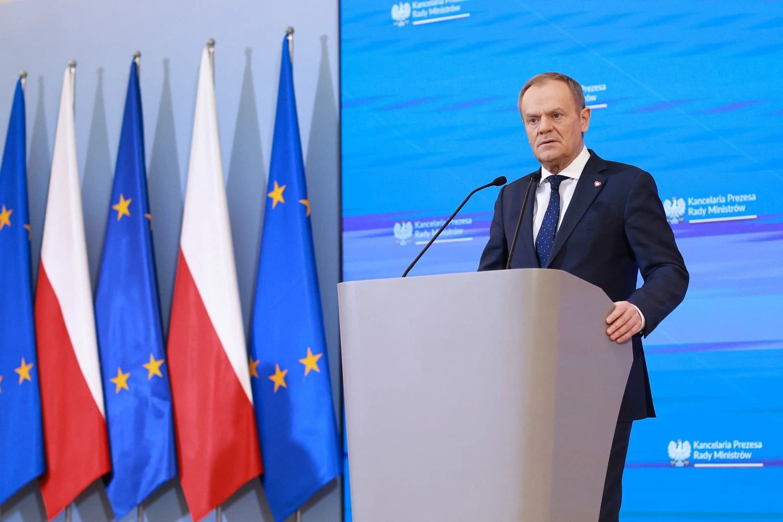 Donald Tusk, Prime Minister of Poland, speaking at a press conference with flags.
